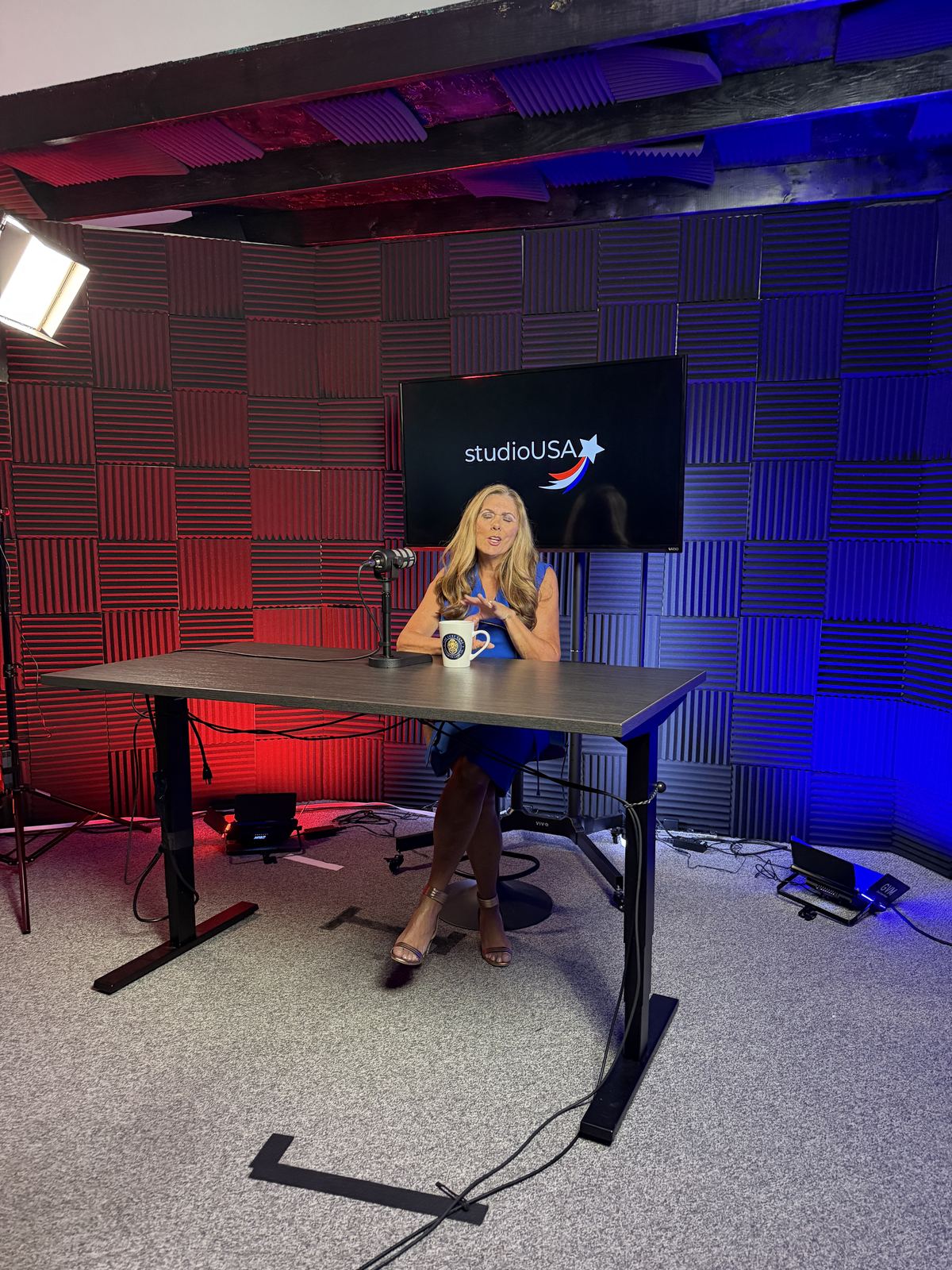 Guest seated at the desk on the red and blue studioUSA set with a branded screen behind her