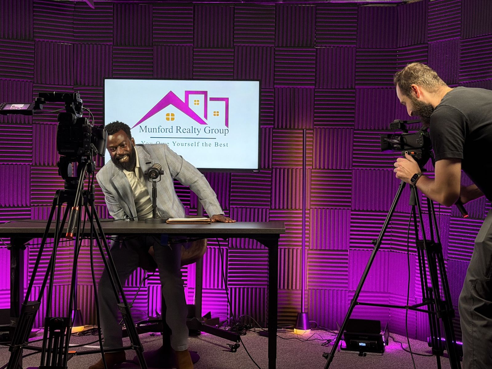 Camera operator filming a presenter at a desk on the purple set at studioUSA West