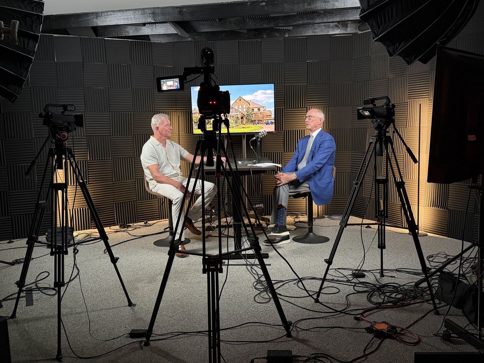 Two guests seated for an interview with three cameras on the gray set at studioUSA West